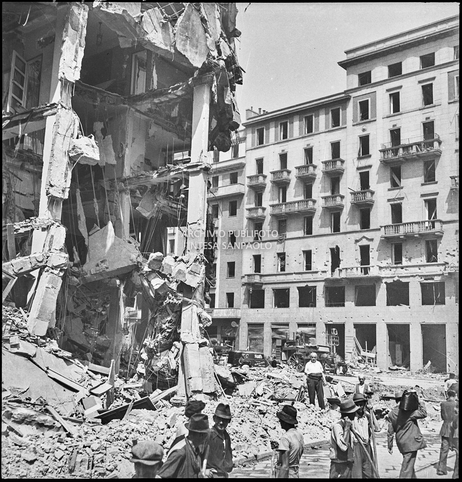 Passanti in via Torino all'angolo con piazza Santa Maria Beltrade, a Milano, davanti a un edificio sventrato dai bombardamenti