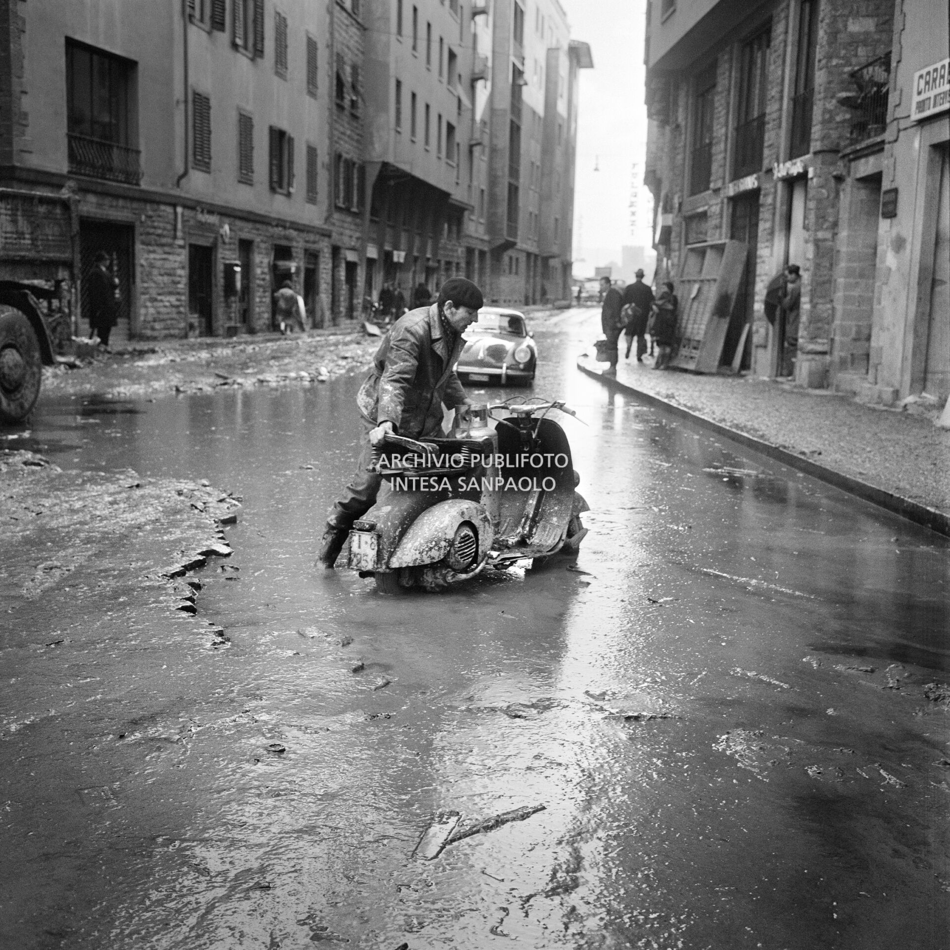 A man pushes a Vespa through the streets of Florence submerged in mud, after the flood