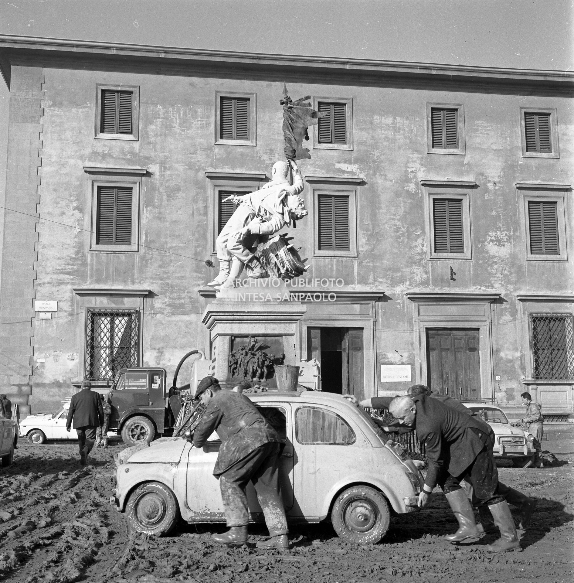 Men pushing a Fiat 500 car in piazza Mentana in Florence after the flood