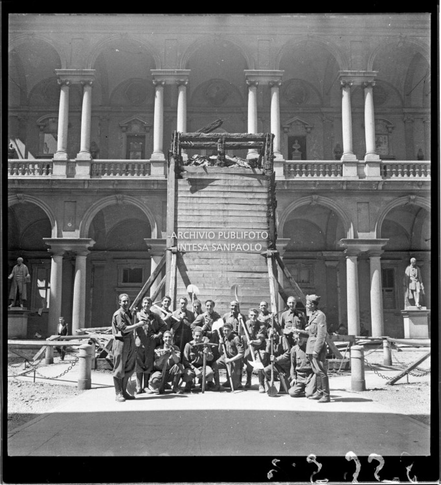 Gruppo di militari ritratto nel cortile d'onore del Palazzo di Brera a Milano, davanti alla statua di Napoleone Bonaparte scampata ai bombardamenti grazie all'ingabbiatura di legno e ai sacchi di sabbia messi a protezione preventiva