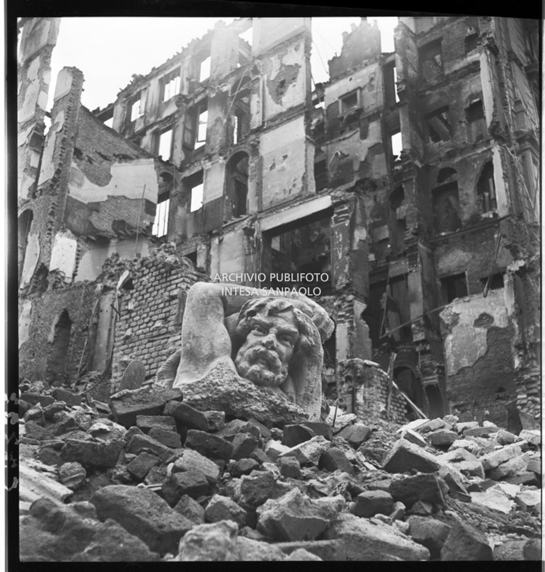 La testa di un telamone giace su un cumulo di macerie degli edifici sventrati dai bombardamenti tra via Lecco e via San Gregorio a Milano