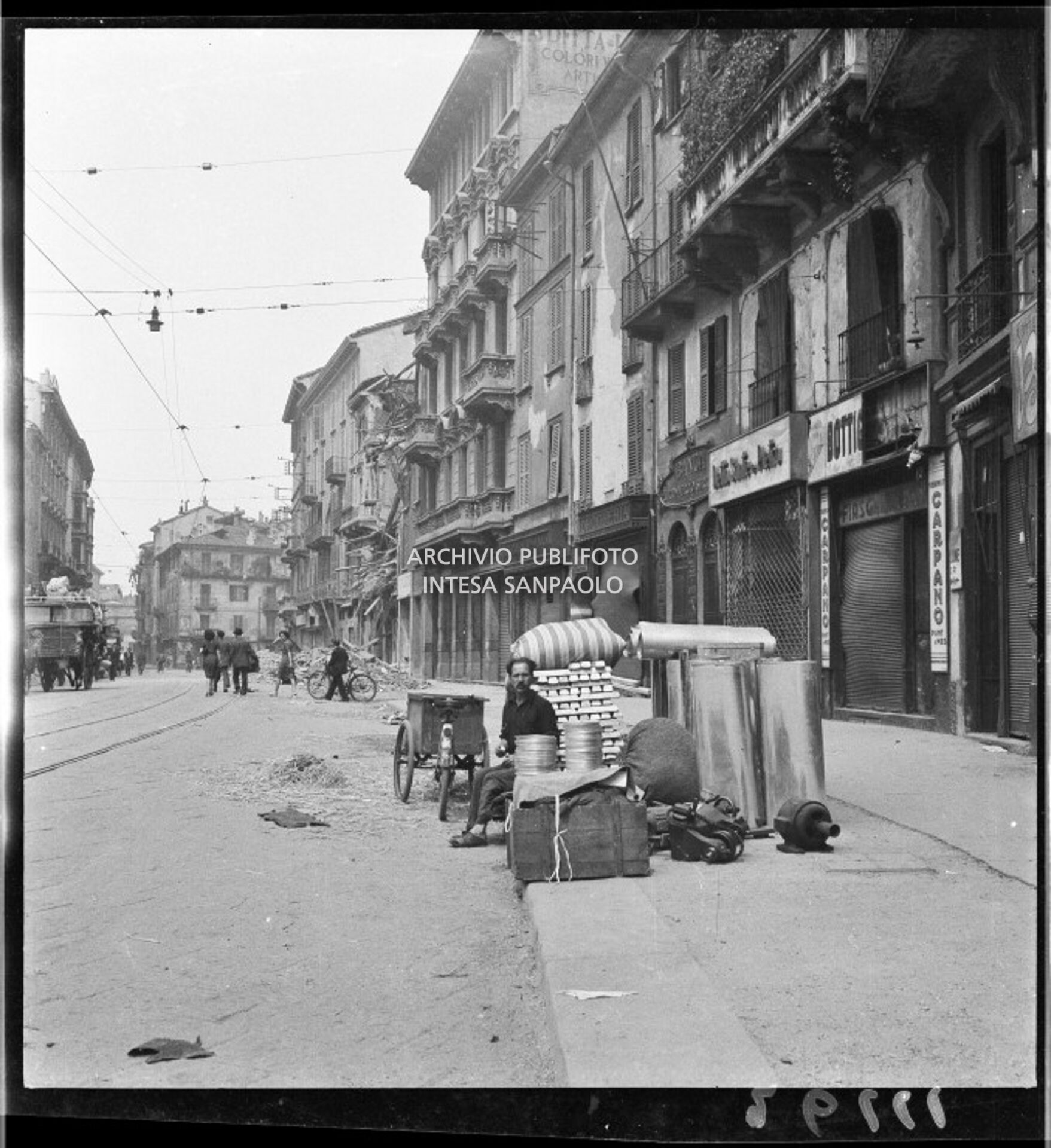 Via Ponte Vetero a Milano dopo i bombardamenti: sullo sfondo le macerie di un edificio crollato; in primo piano un uomo seduto a fianco a materiale vario