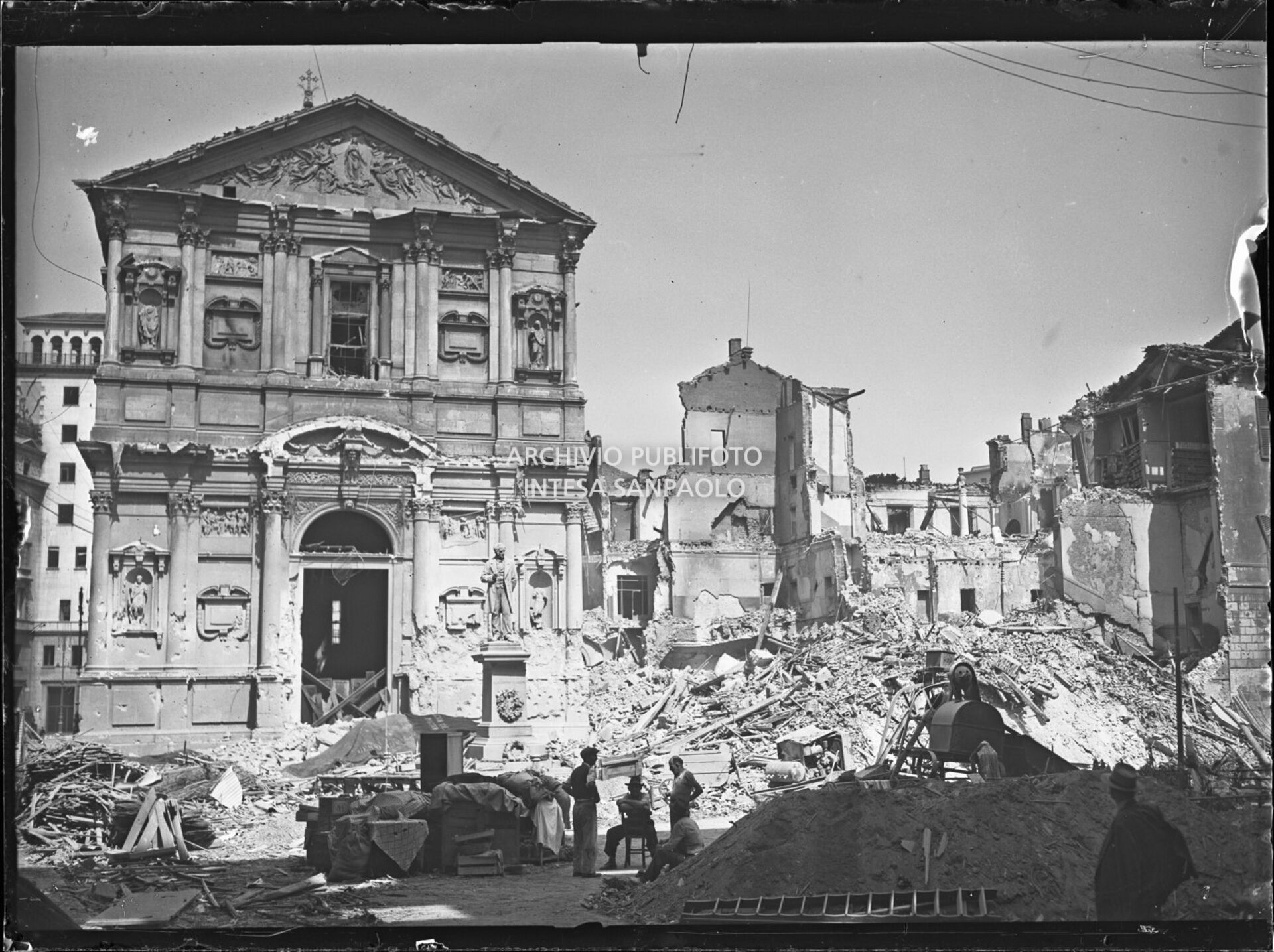 Chiesa di San Fedele, nell'omonima piazza a Milano, gravemente danneggiata dai bombardamenti; sulla destra l'edificio che ospitava la questura della città, completamente distrutto; davanti alla chiesa il monumento a Alessandro Manzoni intatto