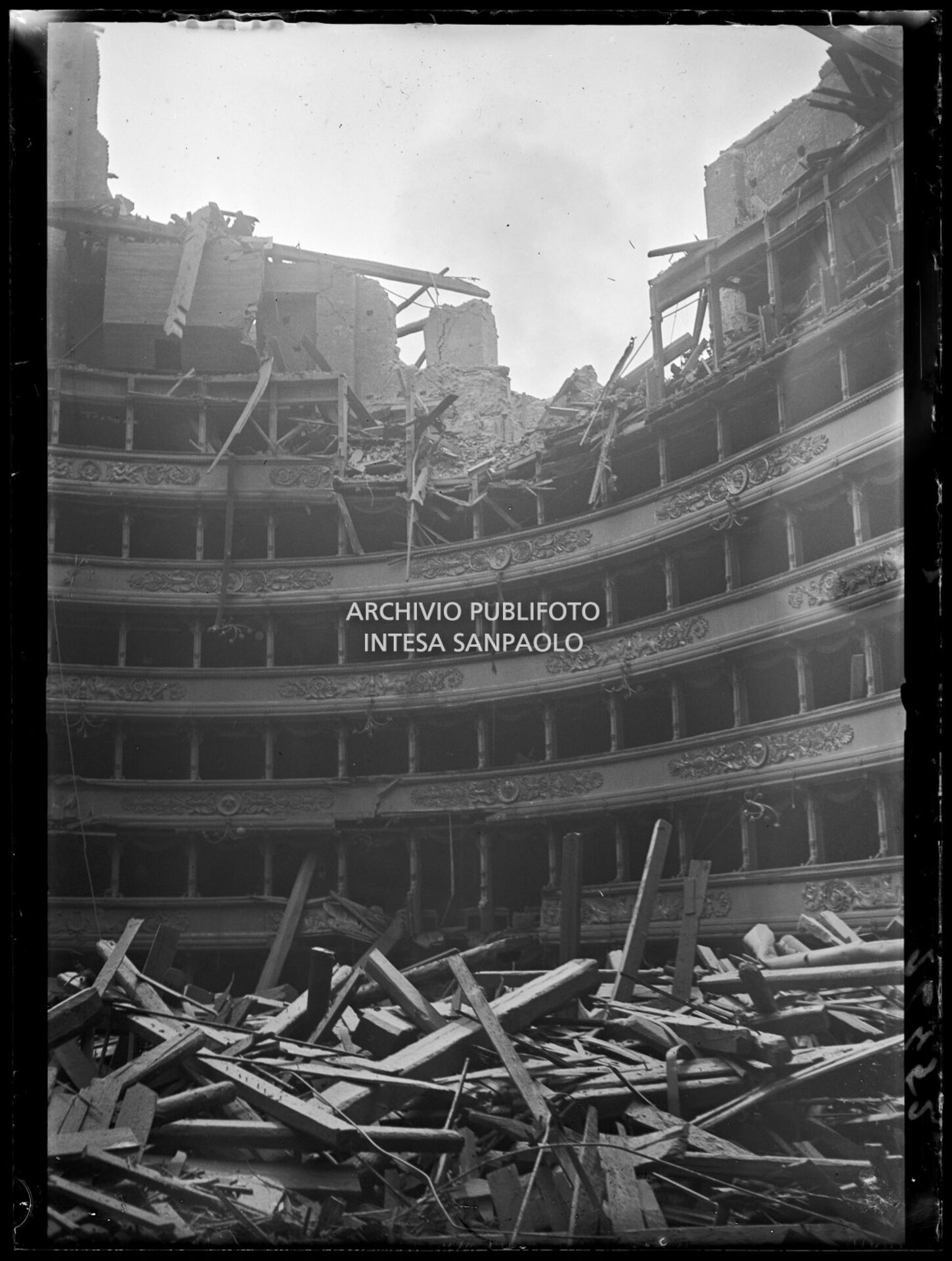 Interno del Teatro alla Scala di Milano dopo i bombardamenti: il tetto e la volta centinata sottostante sono completamente crollati distruggendo in parte il quinto e sesto ordine di gallerie e danneggiando i palchi,  il proscenio e la platea
