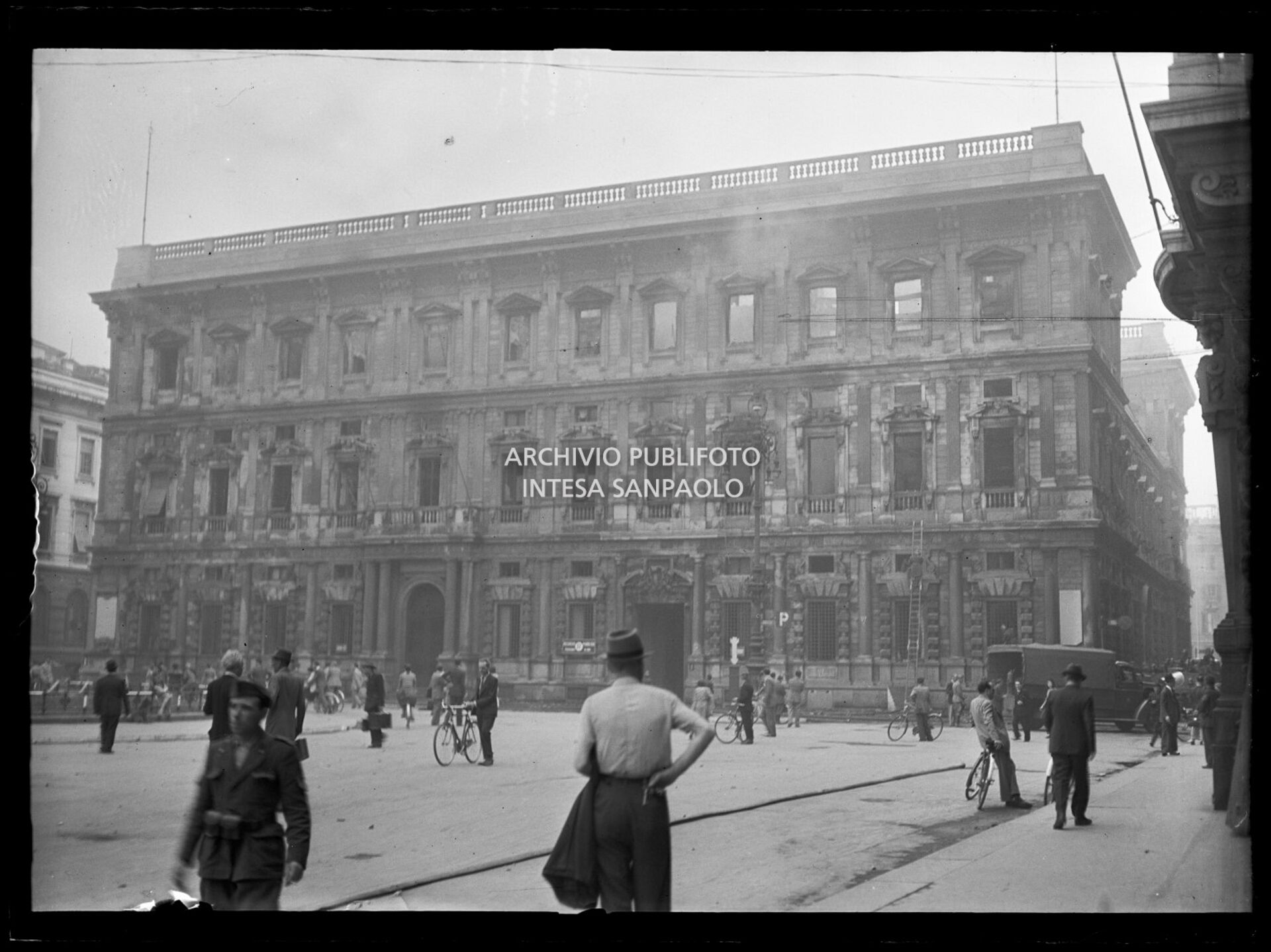 Palazzo Marino, a Milano, completamente bruciato e ancora fumante a causa dei bombardamenti, di cui sono rimasti intatti solo i muri perimetrali. Sulla destra l'intervento dei vigili del fuoco
