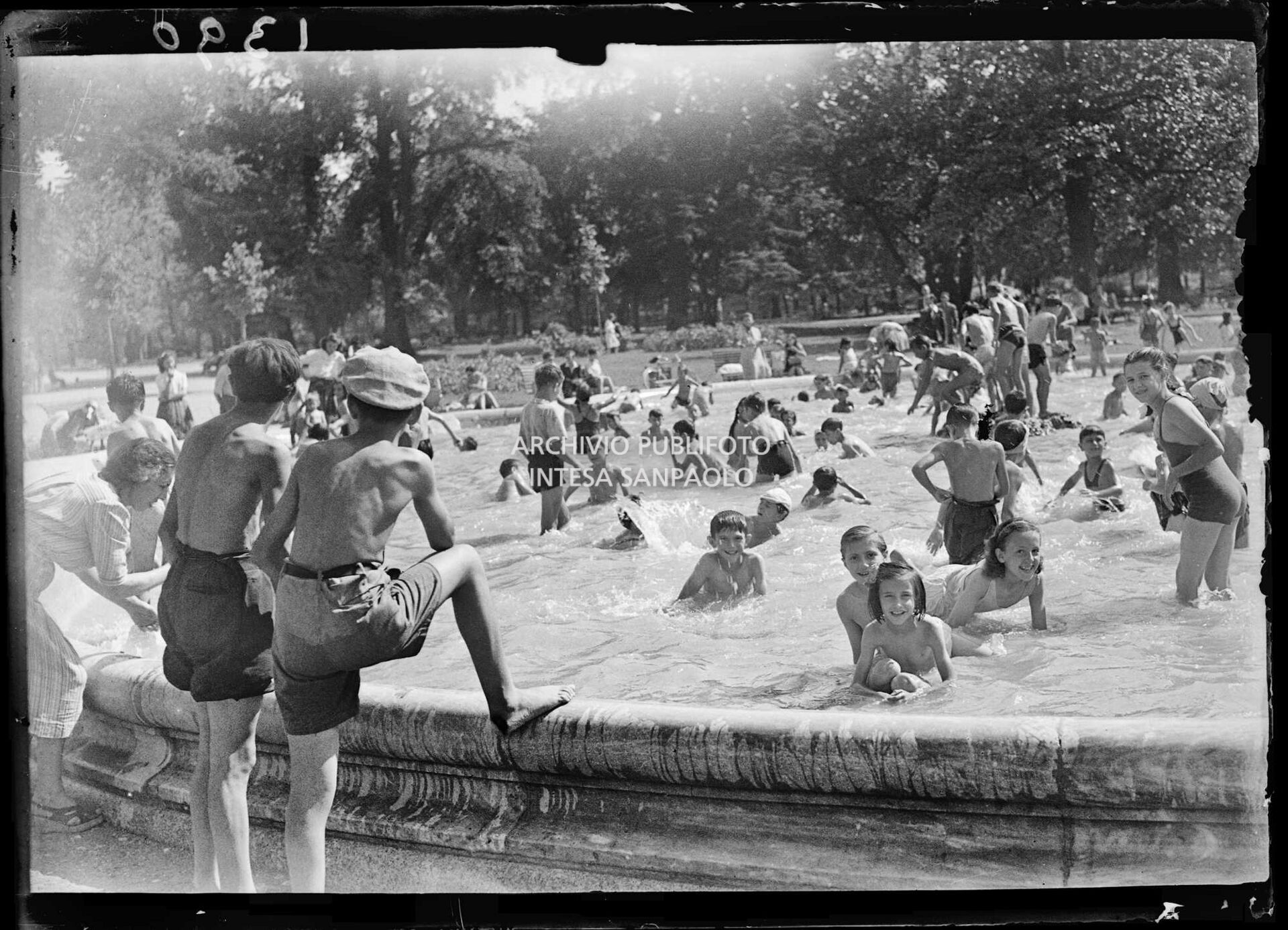 Due ragazzini osservano la fontana dei Giardini Pubblici di Milano utilizzata come piscina dai bambini in occasione di un'eccezionale ondata di caldo estivo