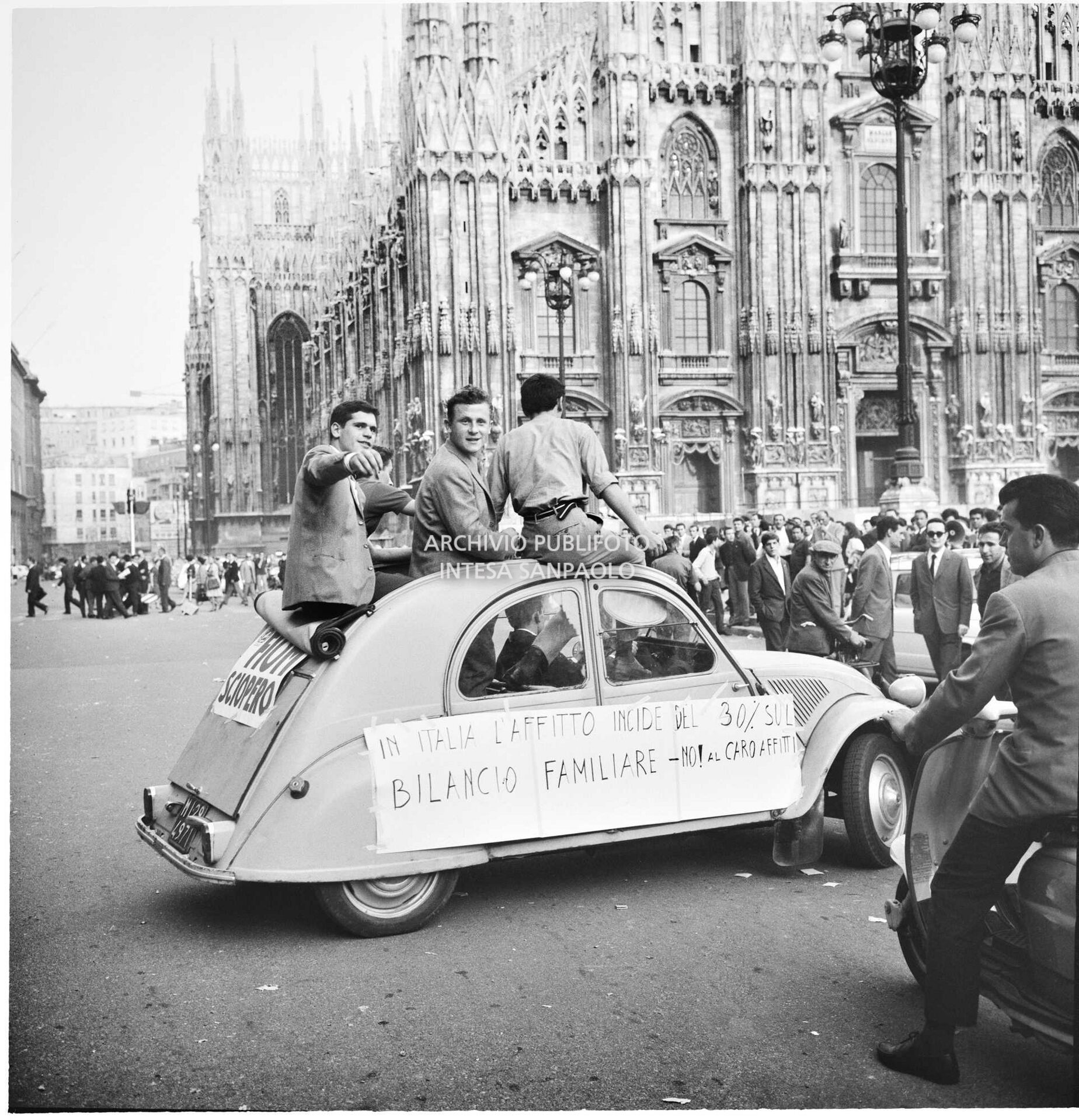 Tre uomini a bordo di una Citroën 2CV, in piazza del Duomo a Milano, durante una manifestazione contro la speculazione edilizia