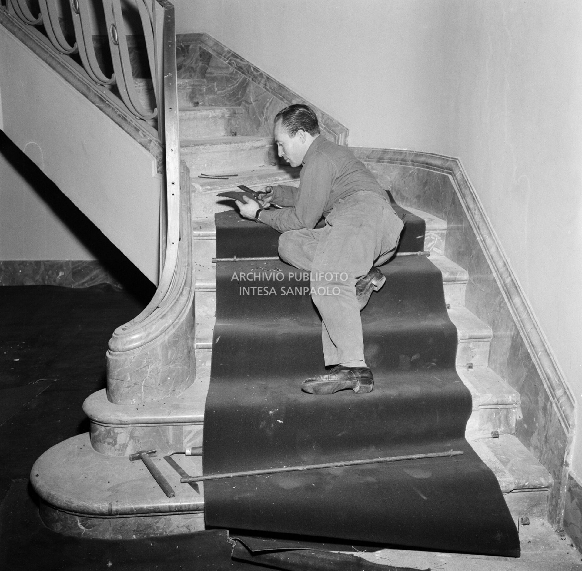 Operaio allestisce la passatoia lungo una scalinata, all'interno del Teatro alla Scala, in preparazione della serata inaugurale della stagione lirica 1957-1958