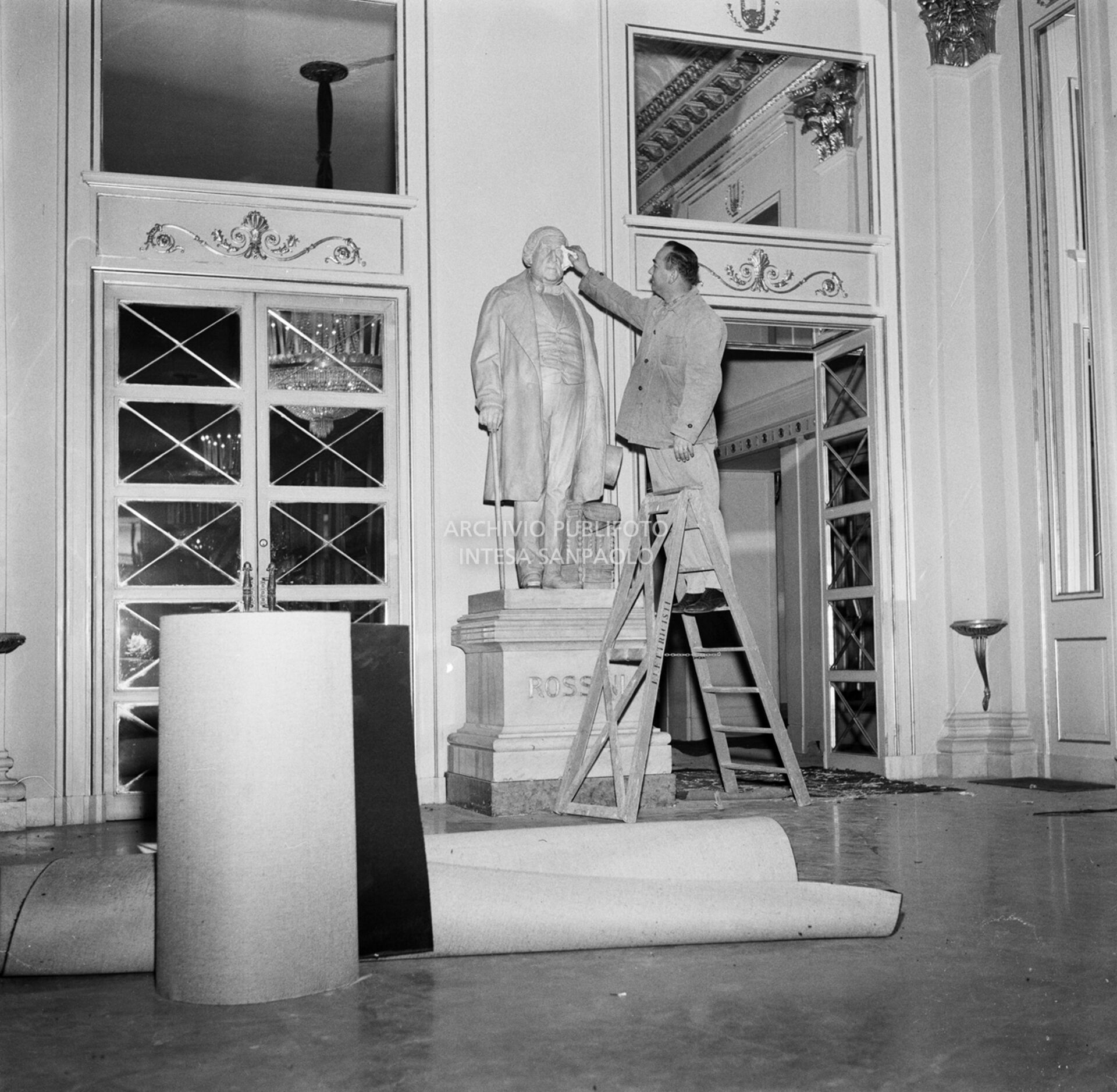 Addetto alle pulizie spolvera la statua di Gioachino Rossini, esposta nel foyer del Teatro alla Scala, in vista dell'inaugurazione della stagione lirica 1957-1958