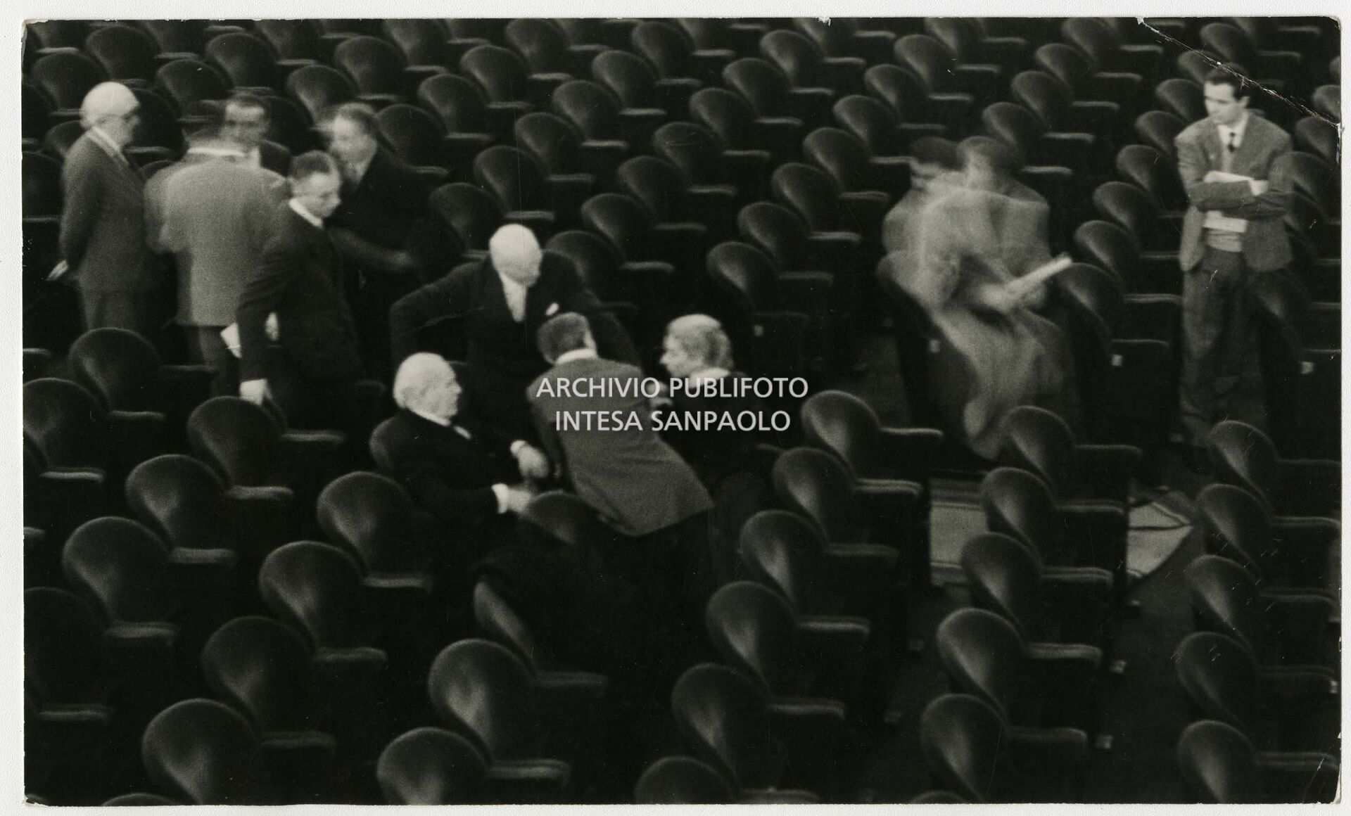 Original caption by Publifoto Agency on the back of the print:
			"And everyone felt really small.
			A historical photo. Milan, 1 December 1954. 
			This historic photograph shows Maria Callas with three great conductors: Arturo Toscanini, Victor De Sabata and Antonino Votto. The photograph was taken on 1 December 1954, when Toscanini wanted to attend one of the last rehearsals of La Vestale that would open the Milan opera season on the 7th of December that year. The maestro lingered in the stalls for a long time and then wanted to talk to Callas. As can be clearly seen in photo 237189 (Antonino Votto from behind), all three conductors are looking towards Callas who is talking about her interpretation of Spontini's opera. Maria Callas' last meeting with Toscanini was in 1955, during rehearsals for Carmen."