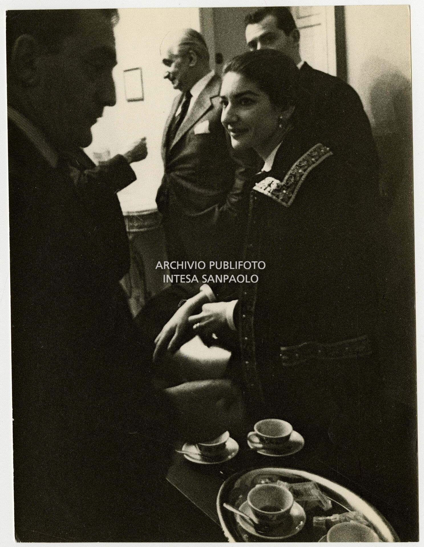 Maria Callas con Luchino Visconti, tra gli altri, dietro le quinte del Teatro alla Scala in occasione delle prove di Anna Bolena; sullo sfondo il marito Giovanni Battista Meneghini