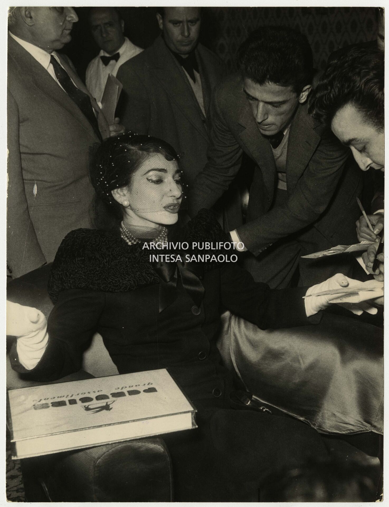 Maria Callas con i giornalisti in occasione della conferenza stampa tenutasi qualche giorno dopo la serata inaugurale della stagione del Teatro dell'Opera di Roma; la soprano, che interpretava la Norma di Bellini, alla fine del primo atto si ritirò in camerino a causa di una brutta raucedine e non rientrò in scena