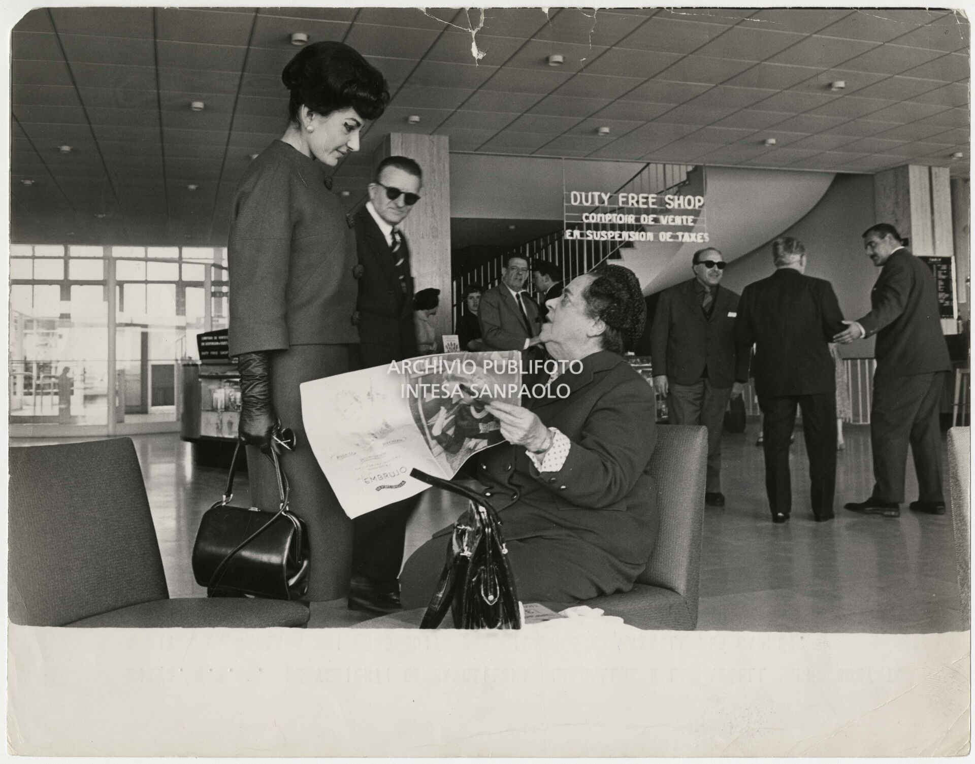 Maria Callas in compagnia di Elsa Maxwell, che le mostra un numero della rivista spagnola "Hola", all'aeroporto di Nizza
