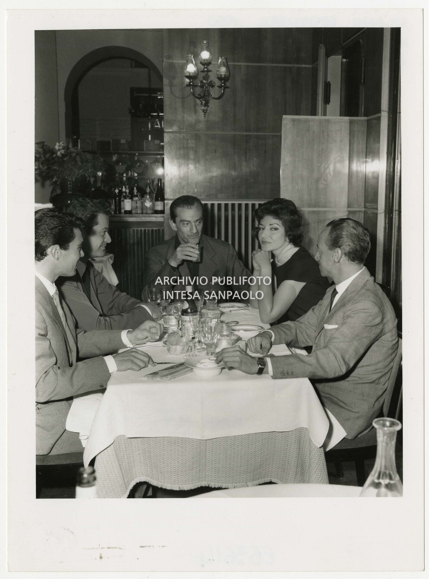 Maria Callas seduta a tavola tra il regista Luchino Visconti, a capotavola, e l'avvocato Emanuele Jacchia, primo a destra, al Biffi Scala a Milano