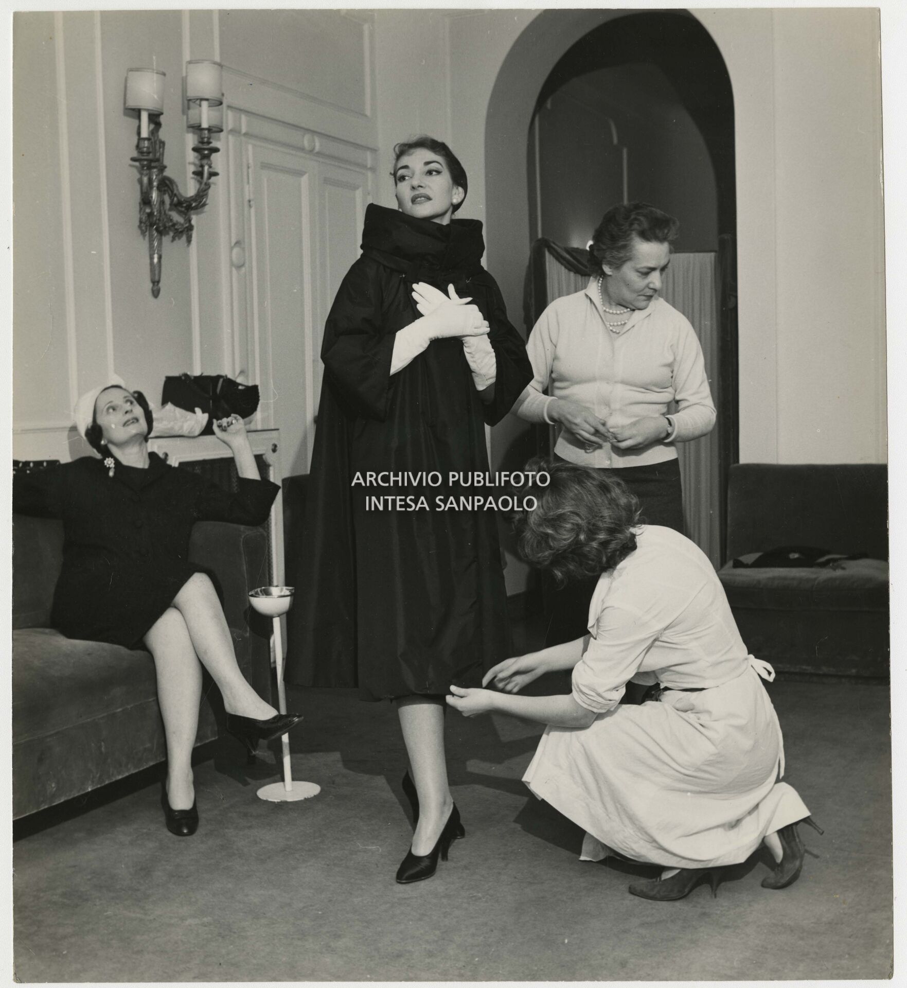 Sarte dell'atelier Biki assistono Maria Callas che prova un soprabito sotto lo sguardo della stilista Elvira Leonardi Bouyeure, detta Biki, seduta sul divano