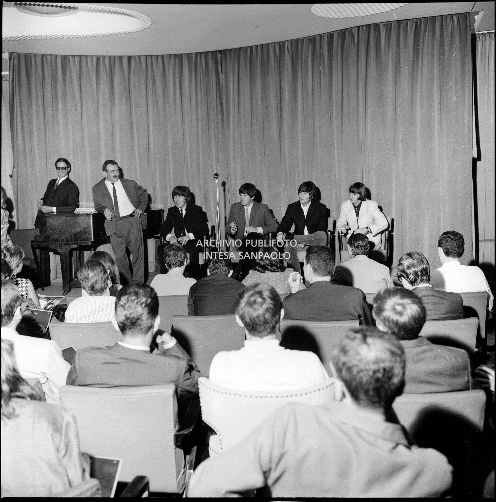 I Beatles in conferenza stampa al Grand Hotel Duomo a Milano: a sinistra in piedi il manager Brian Epstein e a fianco a lui Leo Wächter, l'impresario che portò la band inglese in Italia