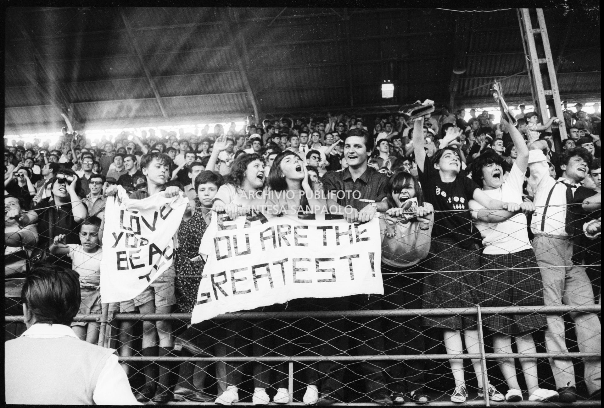 Fan scatenati sugli spalti al concerto pomeridiano dei Beatles al Vigorelli di Milano esibiscono cartelli con scritte "I love you Beatles" e "Beatles you are the greatest", 24 june 1965, Cossu, Sergio, Pavone, Eugenio, Publifoto