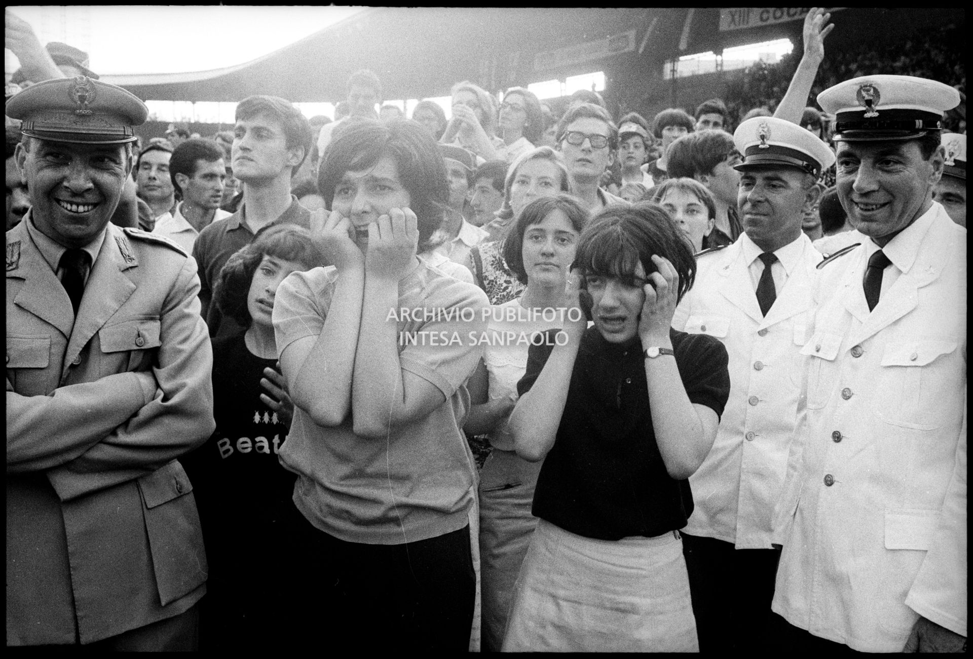 Ragazze, tra il pubblico al concerto pomeridiano dei Beatles al Vigorelli di Milano, urlano per l'entusiasmo; i poliziotti della sicurezza sorridono divertiti, 24 june 1965, Cossu, Sergio, Pavone, Eugenio, Publifoto