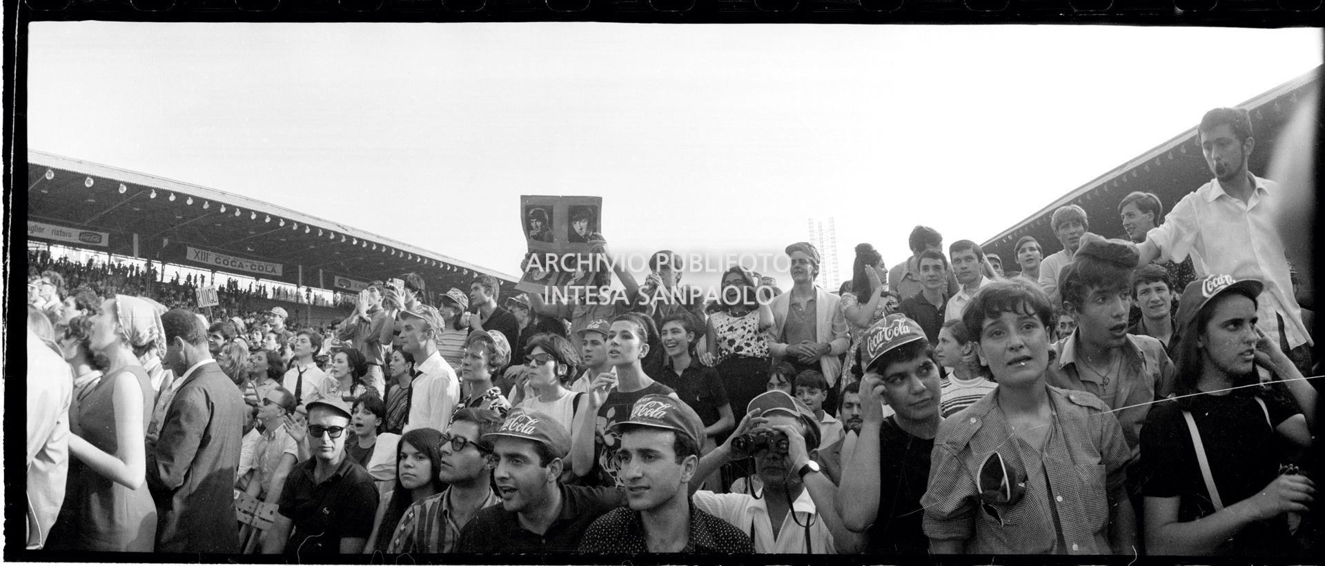 Panoramica del pubblico al concerto pomeridiano dei Beatles al Vigorelli di Milano; un ragazzo mostra una fotografia dei musicisti, 24 june 1965, Cossu, Sergio, Pavone, Eugenio, Publifoto