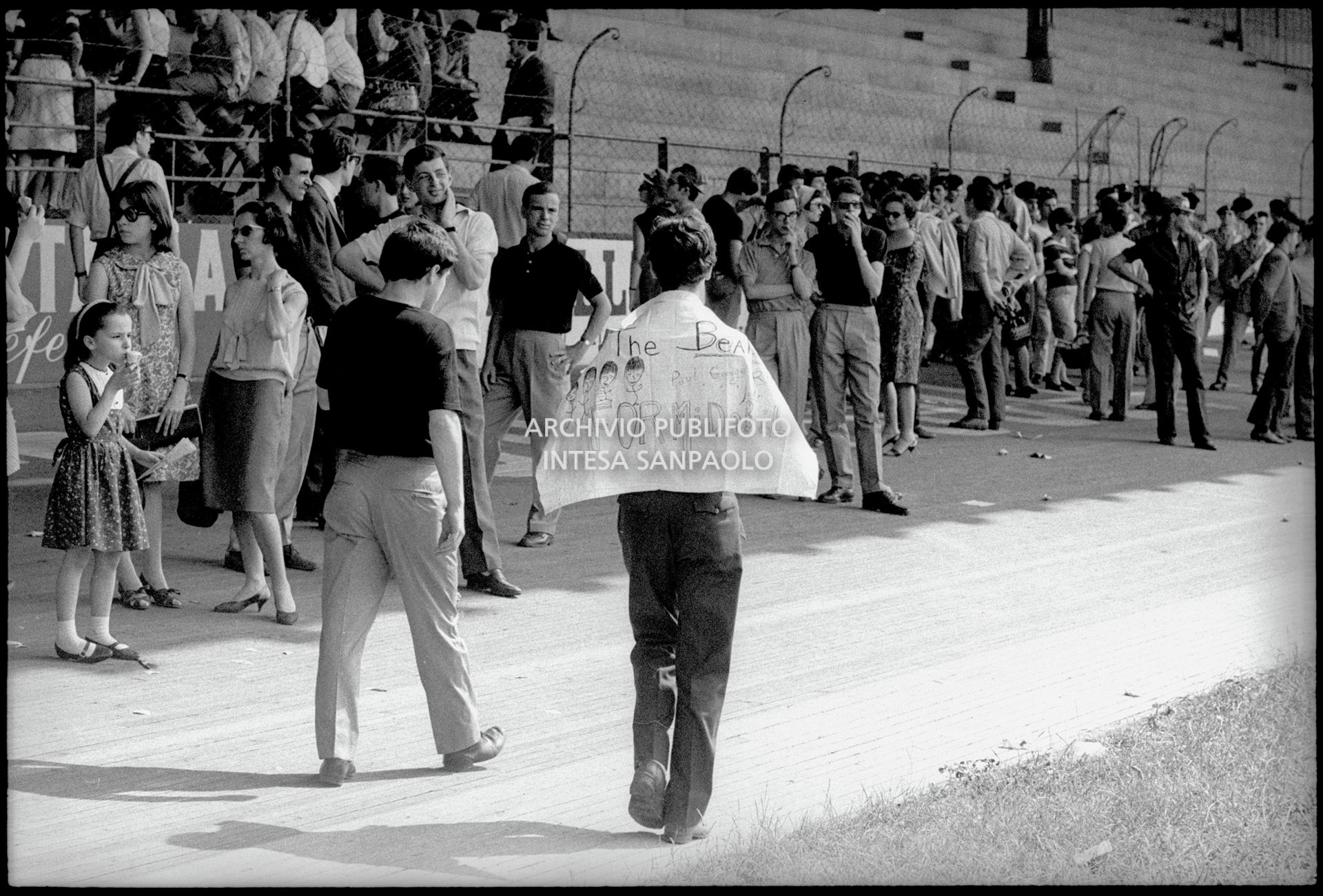 Pubblico cerca riparo all'ombra in attesa dell'inizio del concerto pomeridiano dei Beatles al Vigorelli di Milano, 24 june 1965, Cossu, Sergio, Pavone, Eugenio, Publifoto