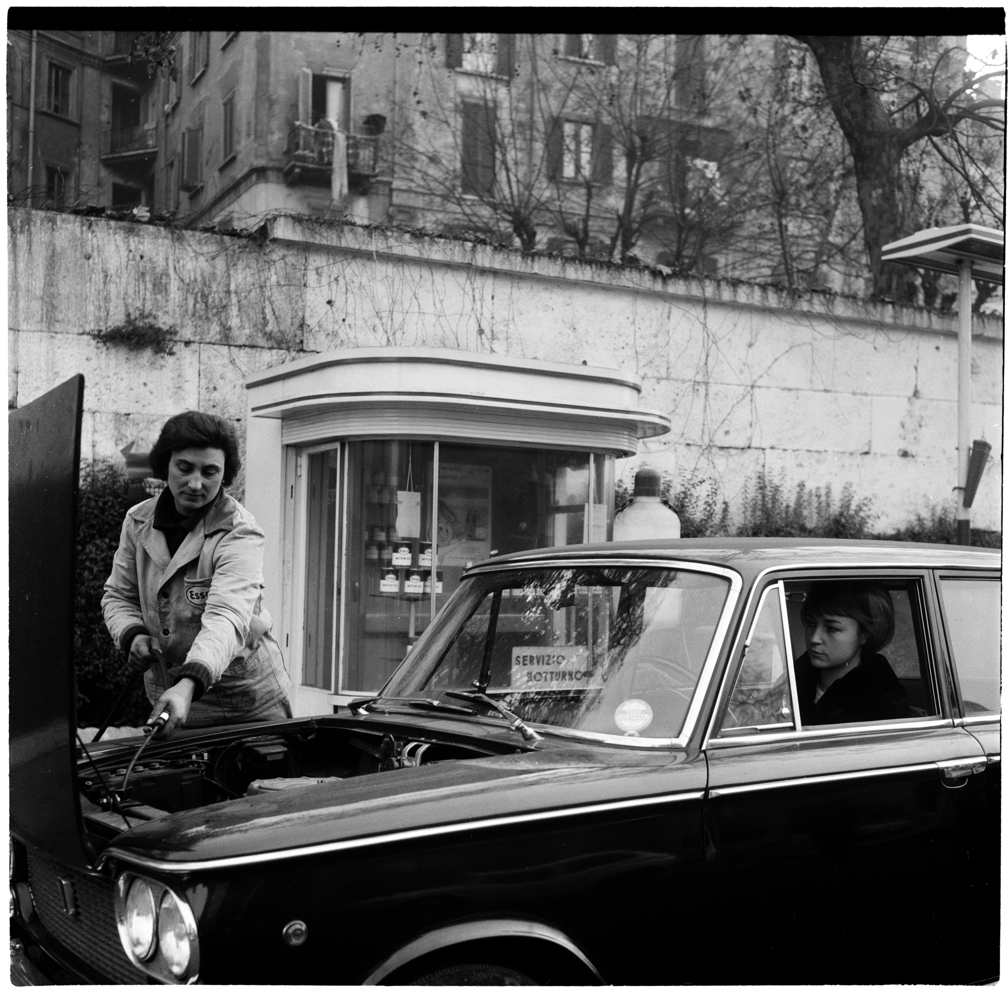 Female petrol pump attendant checks the oil in a car driven by a woman, Milan, 3 November 1962